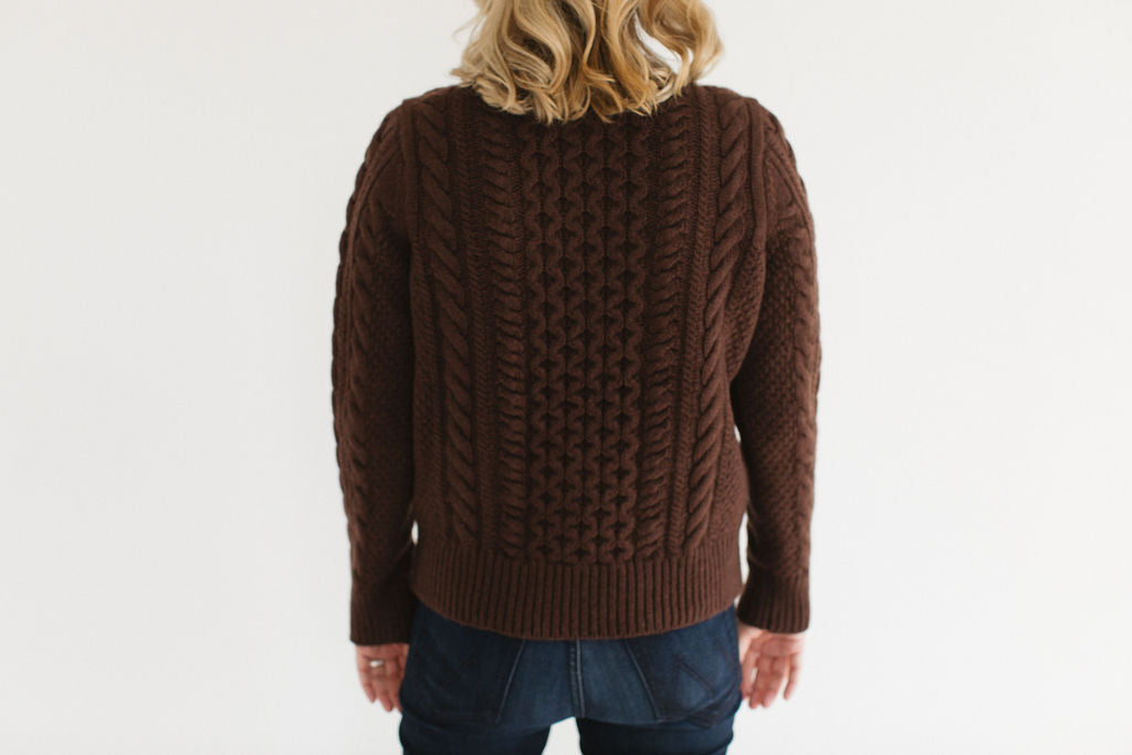 Back view of Eleanor Leftwich wearing the cable knit Fisherman Crewneck in chocolate, paired with dark jeans, against a white background.