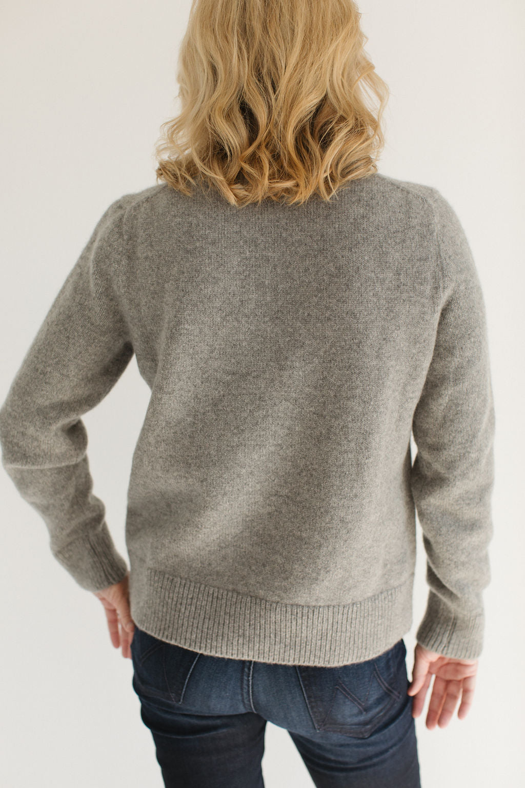 Back view of Eleanor Leftwich wearing the Gray Classic Cashmere Crew, paired with dark jeans and standing against a white background.