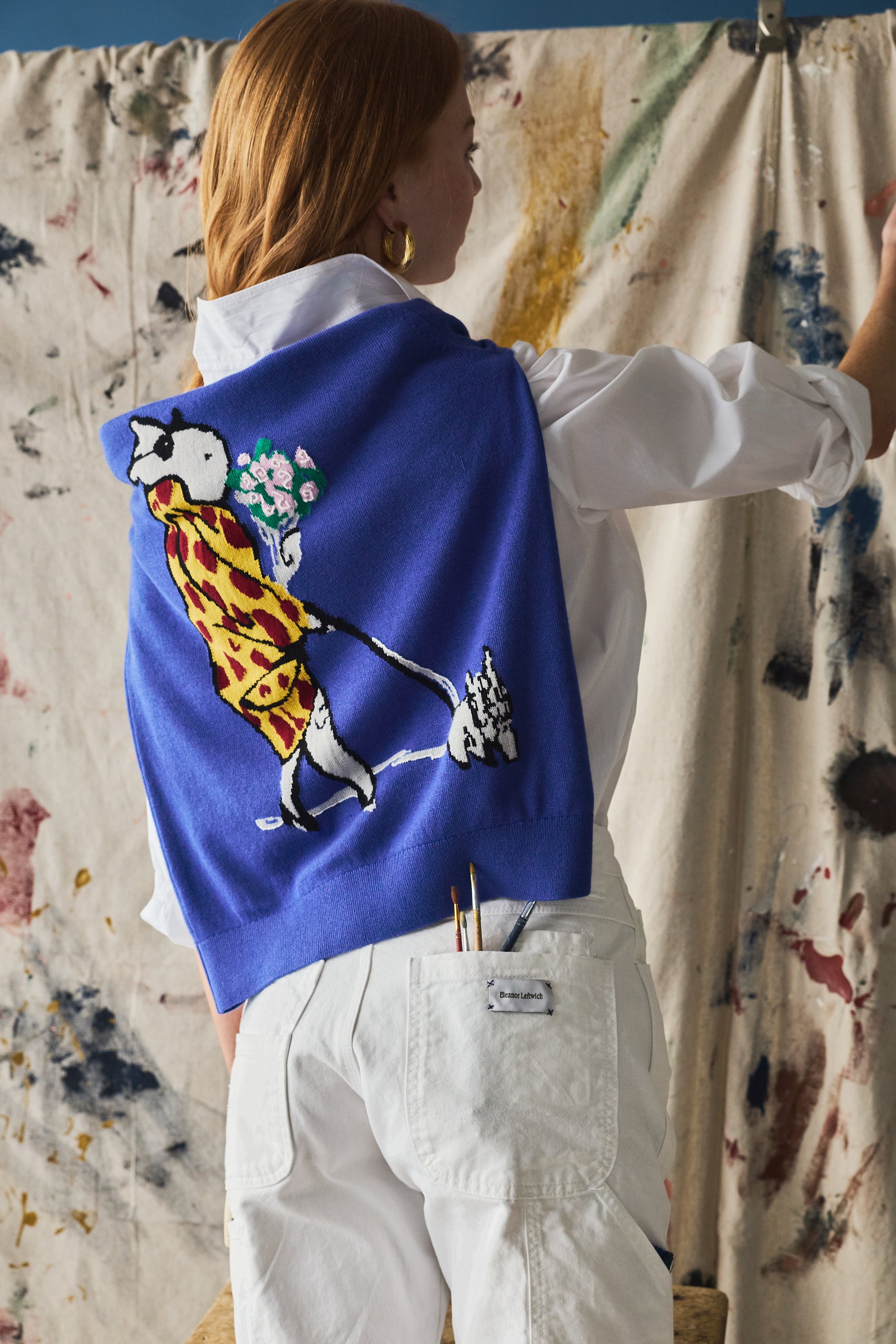 Person wearing a blue sweater with a colorful design, standing in front of a textured wall.