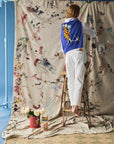 Person standing on a ladder against a large painted backdrop with a blue sweater with a character design on her back