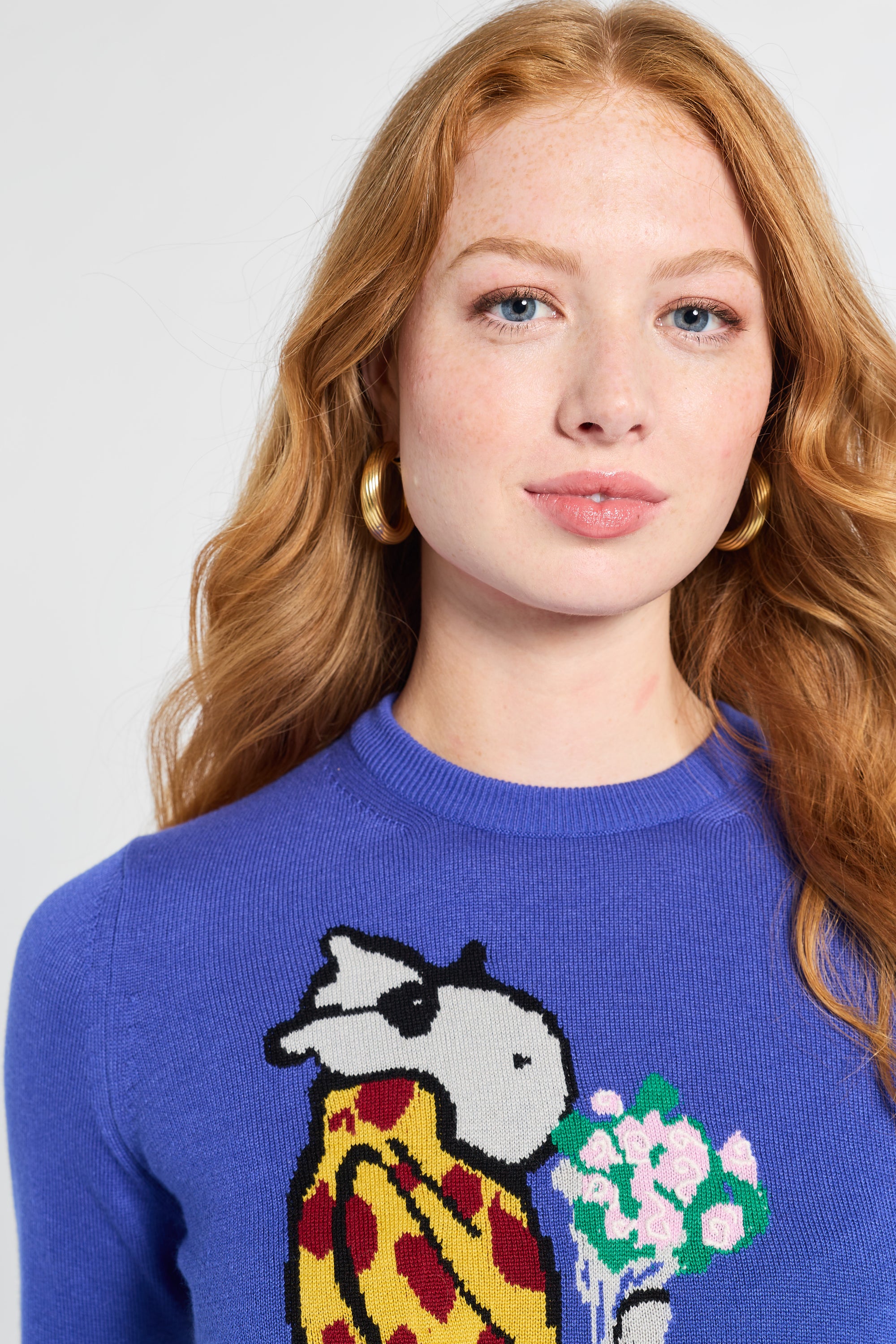 Woman wearing a blue sweater with a colorful design of a hippo and flowers on a white backdrop