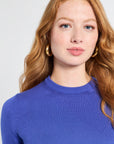 Woman modeling a royal blue sweater with gold hoops against a white background