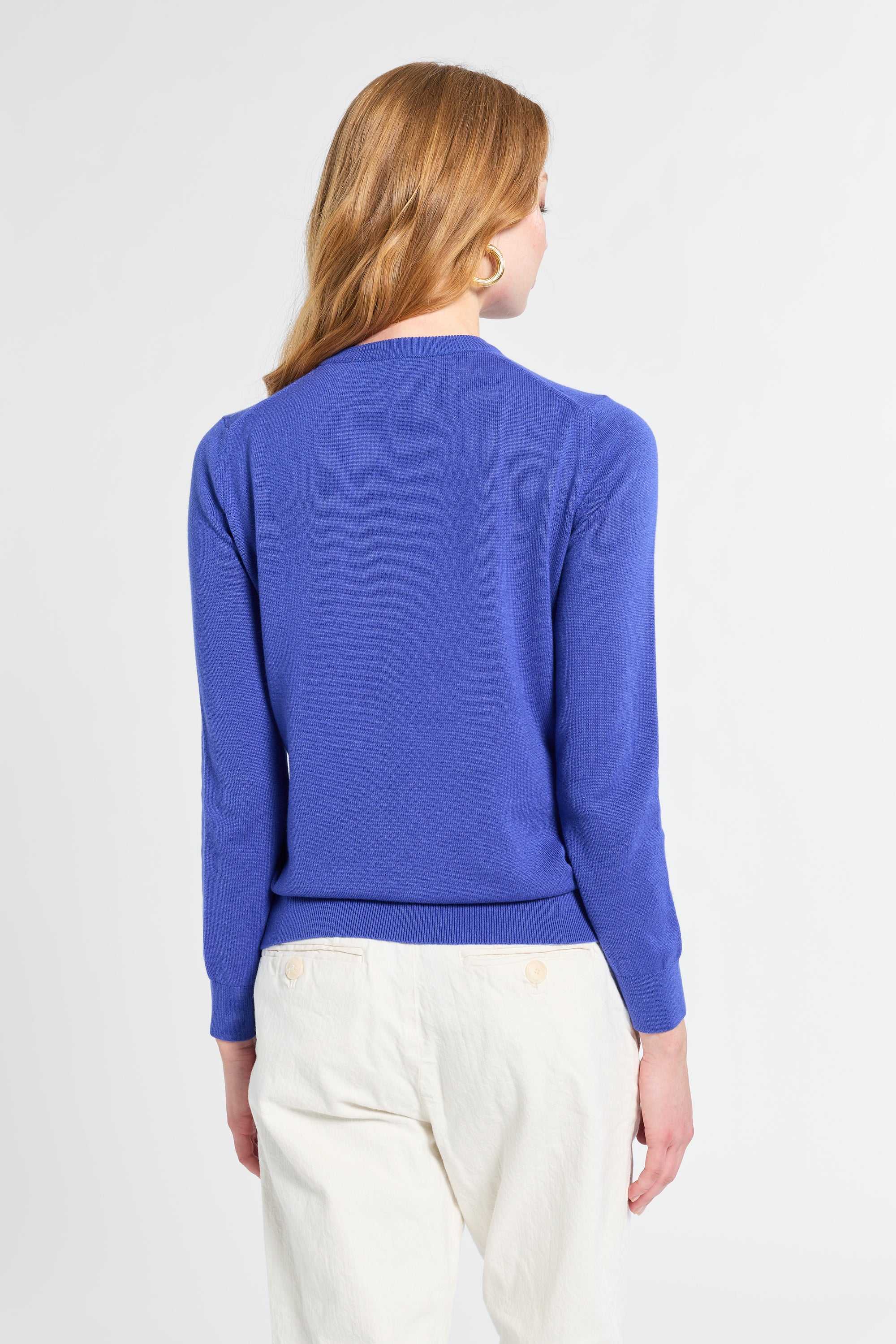 Person wearing a blue sweater and white pants on a plain background
