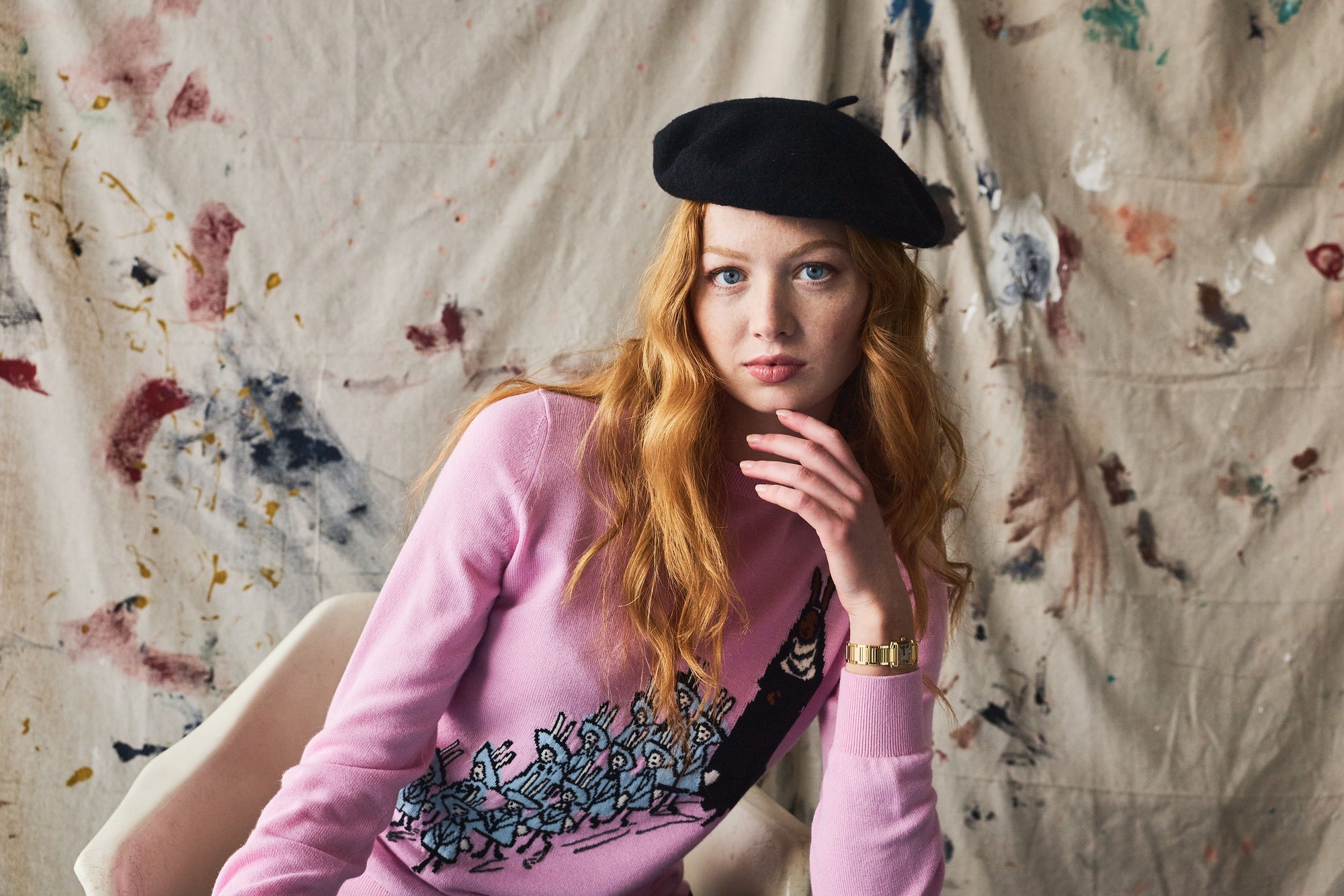 Woman wearing a pink sweater with a black beret against a textured wall.
