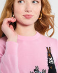Person wearing a pink sweater with knitted designs on a plain background