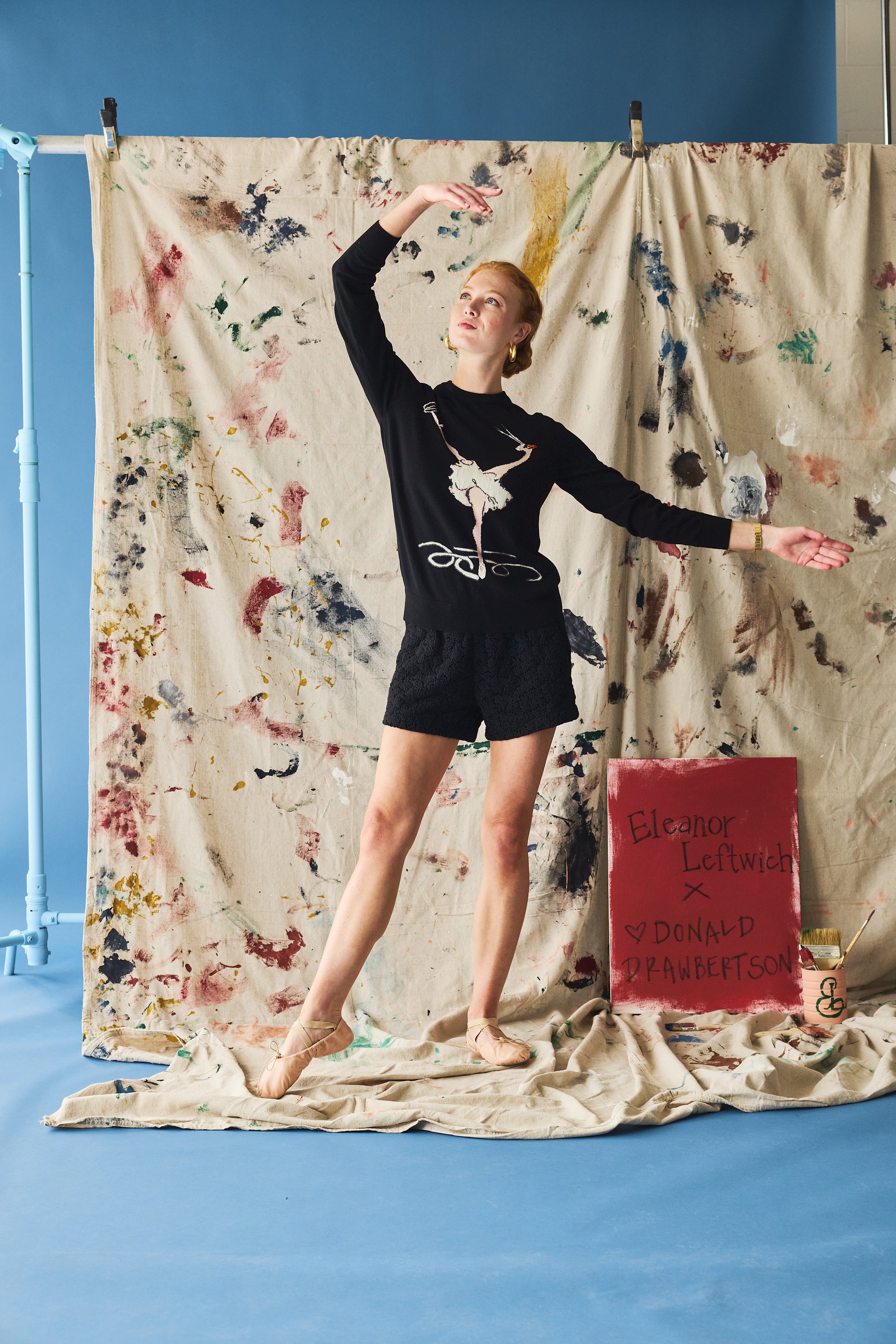 Person in a black outfit with a ballet design standing in front of a colorful curtain.