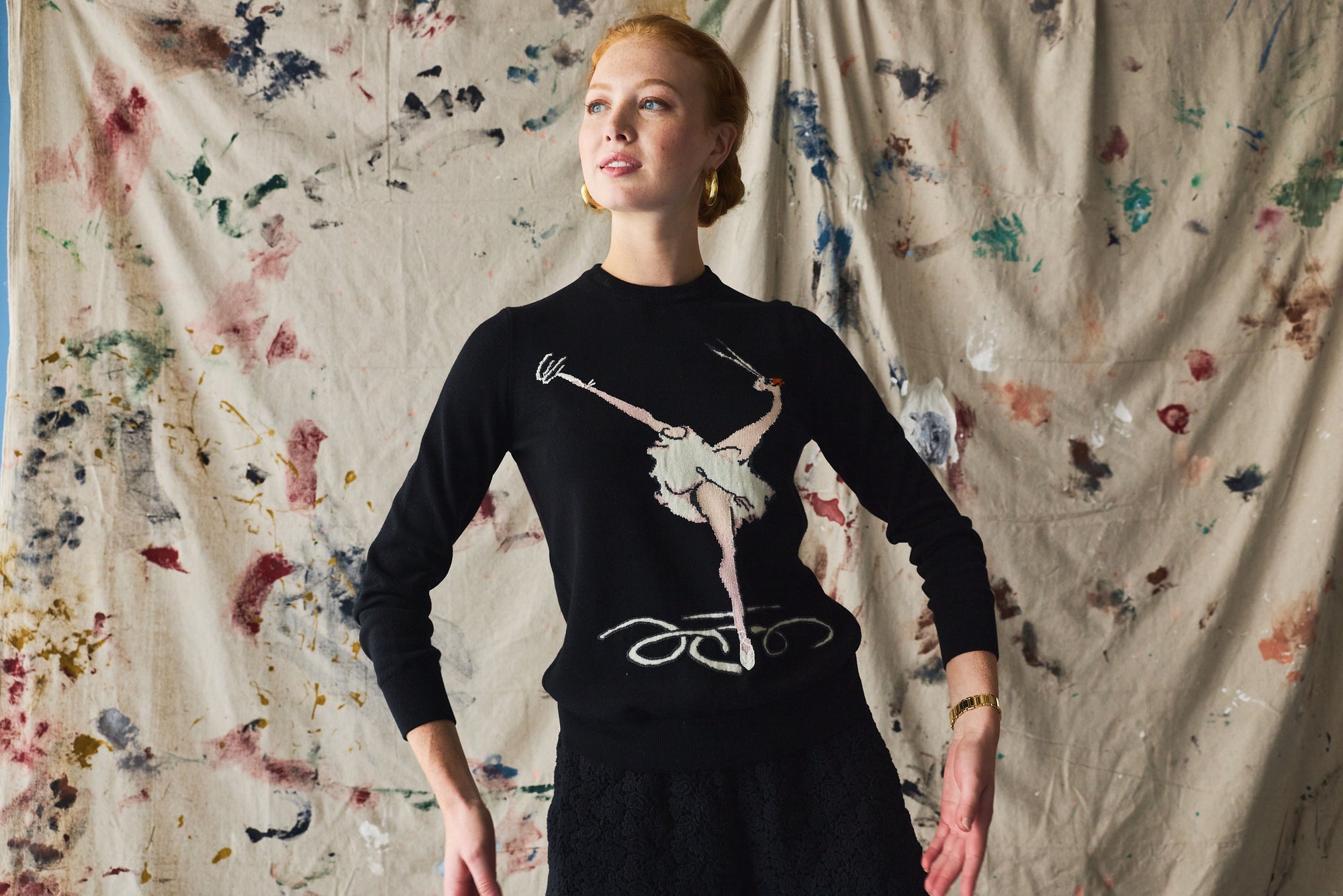 Woman wearing a black sweater with a graphic design against a textured wall.