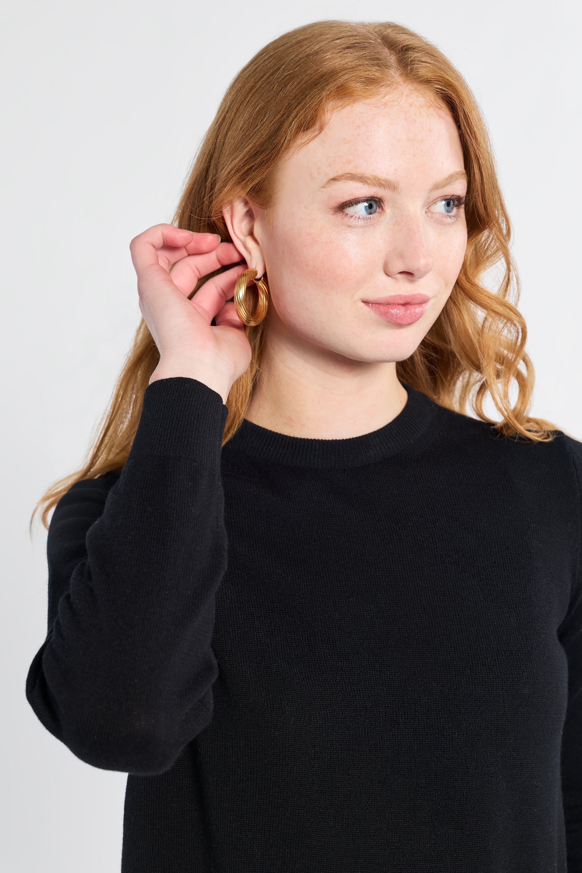 Woman modeling a long sleeve black knit sweater on a white backdrop