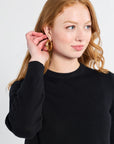 Woman modeling a long sleeve black knit sweater on a white backdrop