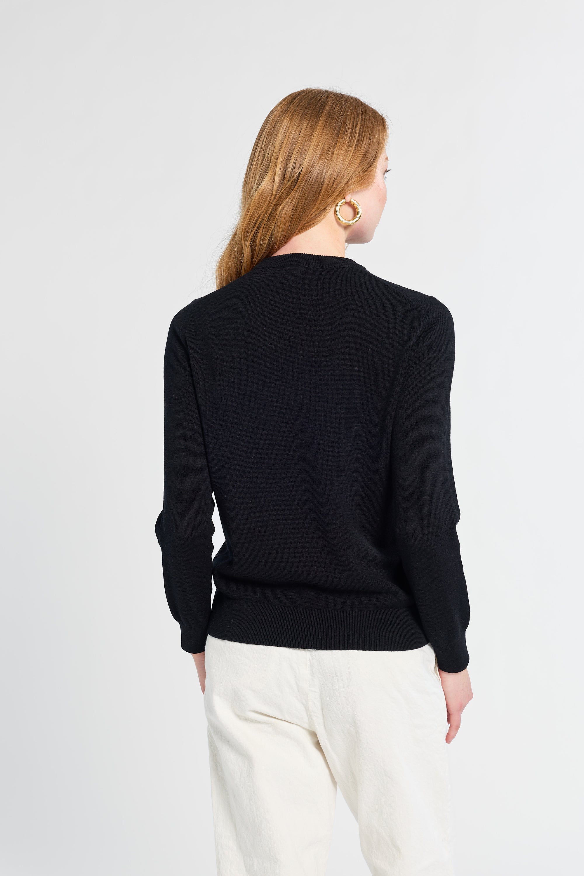 Person wearing a black sweater and white pants on a light gray background
