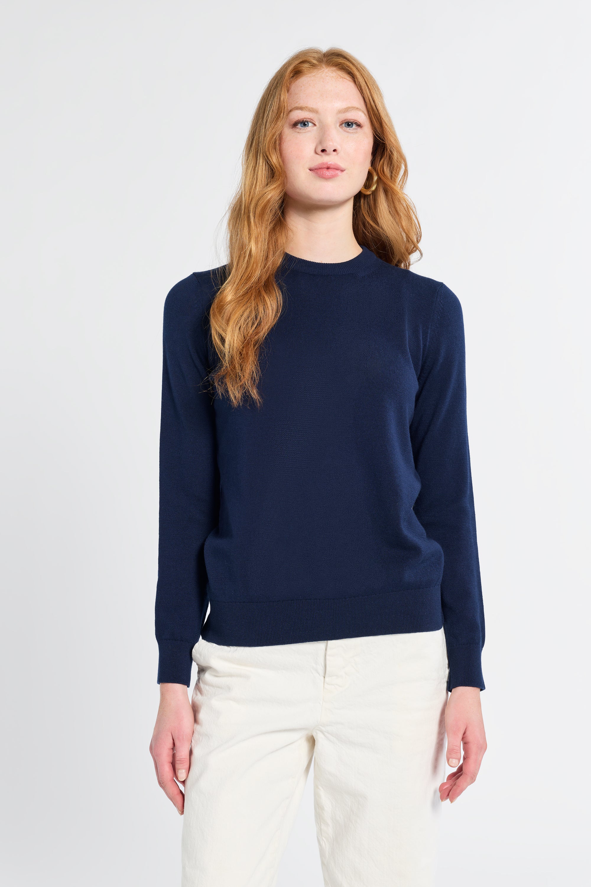 Woman wearing a navy sweater and white pants on a light gray background
