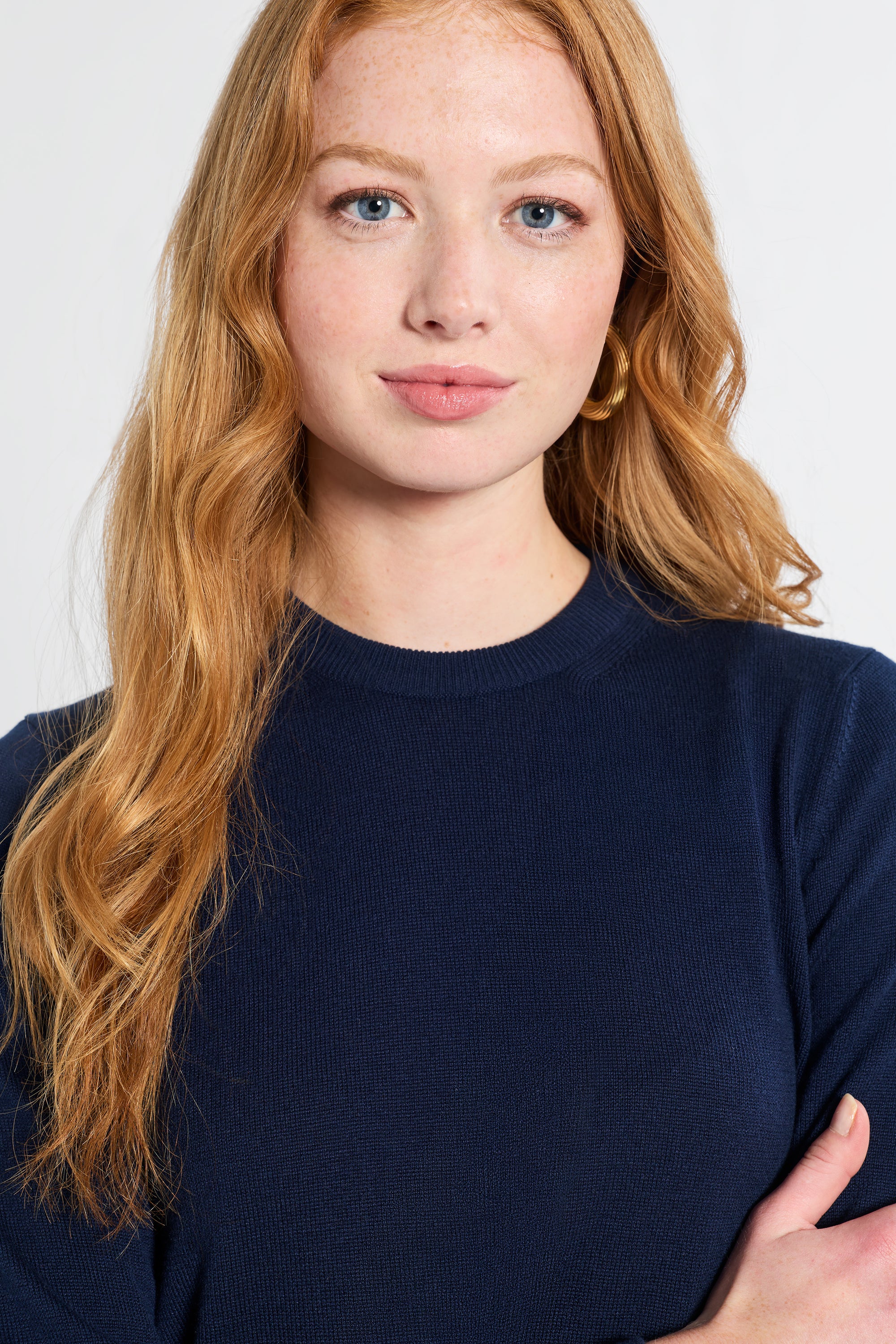 Woman with red hair wearing a navy blue sweater against a white background