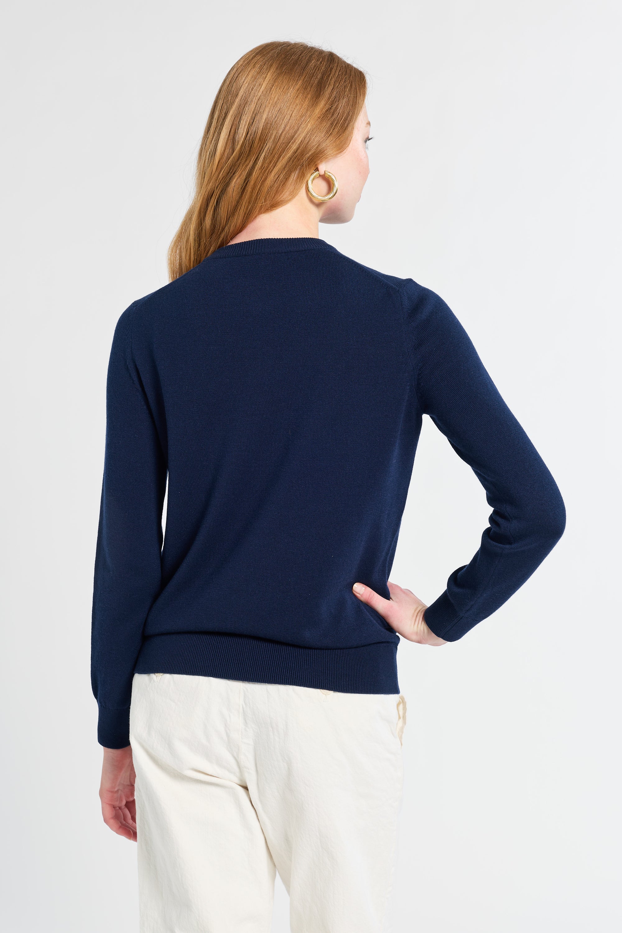 Woman wearing a navy blue sweater and white pants on a white background