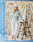 Woman wearing a blue sweater with a giraffe on a sailboat on a paint splotch backdrop