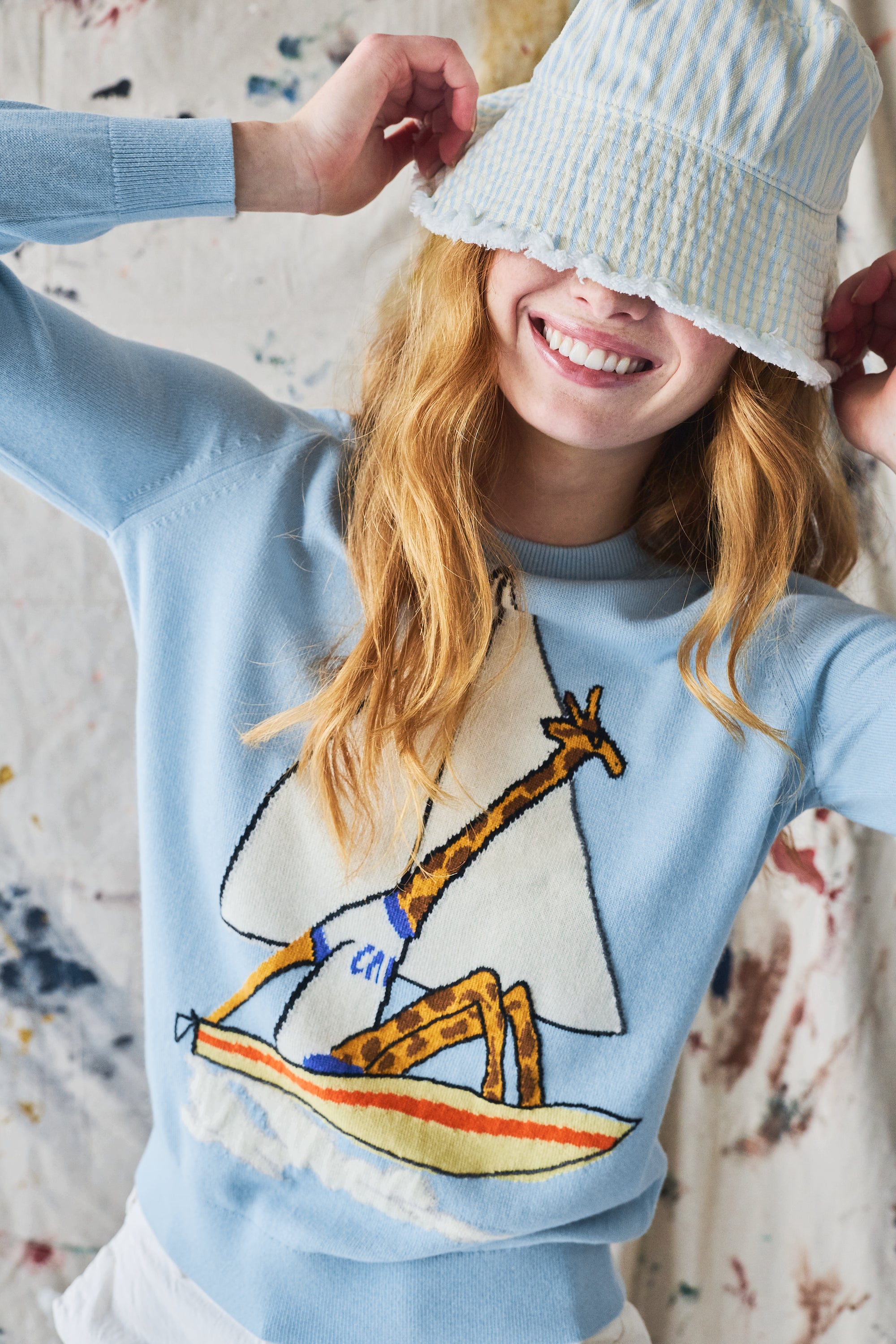 Person wearing a light blue sweater with a sailboat and giraffe design, smiling.