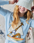 Person wearing a light blue sweater with a sailboat and giraffe design, smiling.