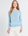Woman wearing a light blue cashmere sweater and white pants on a plain background