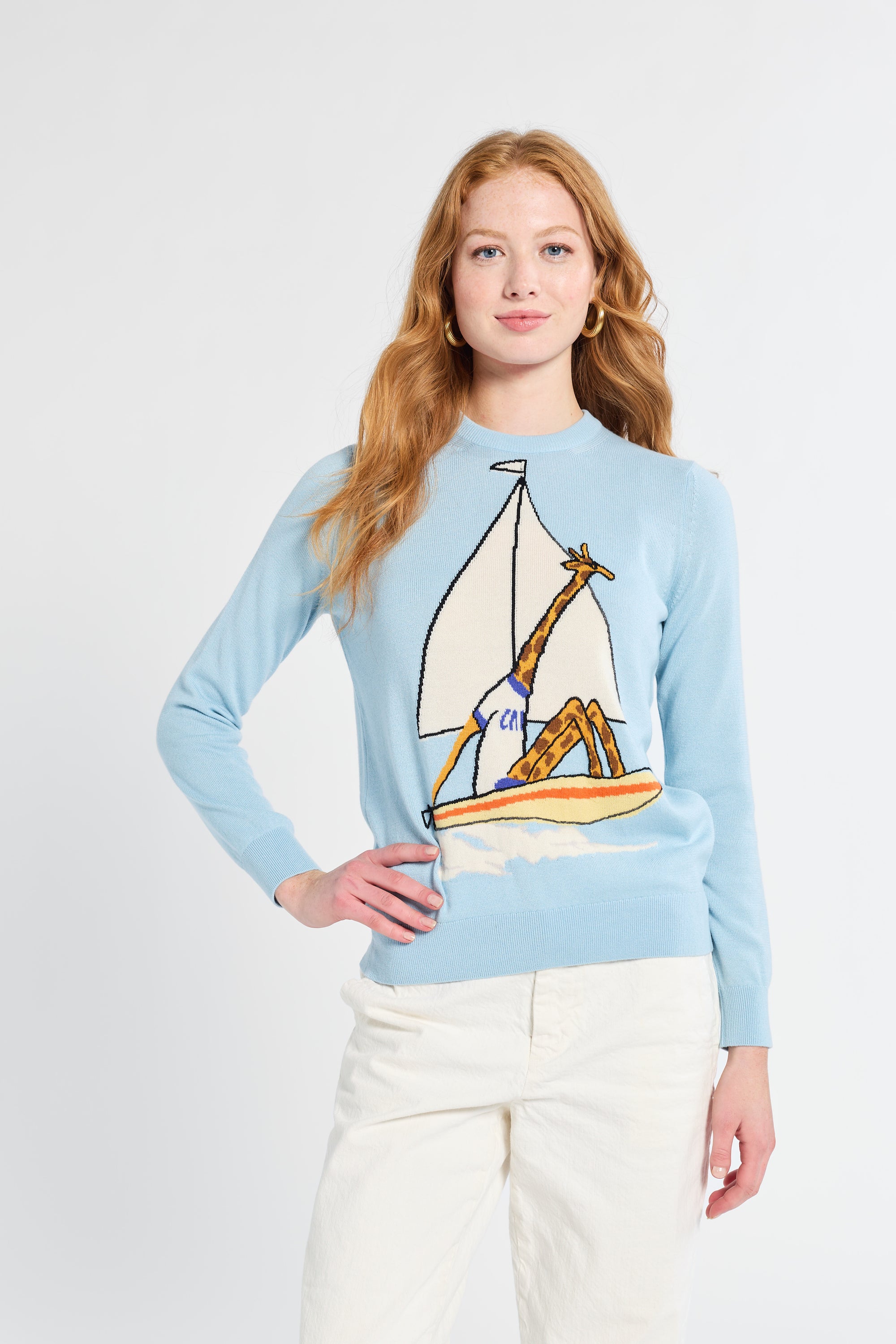 Woman wearing a light blue sweater with a giraffe and sailboat design on a white background