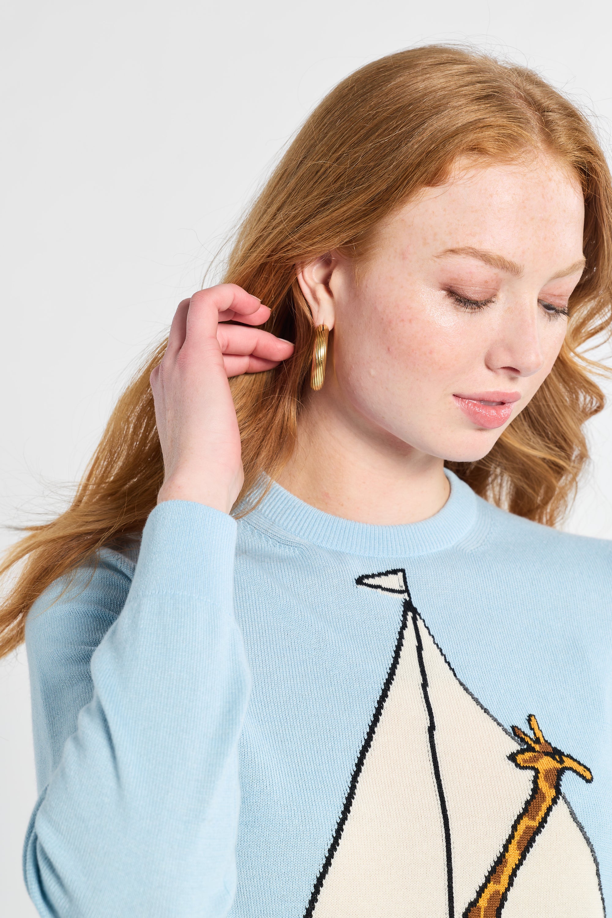 Woman wearing a light blue sweater with a sailboat and giraffe design on a white backdrop