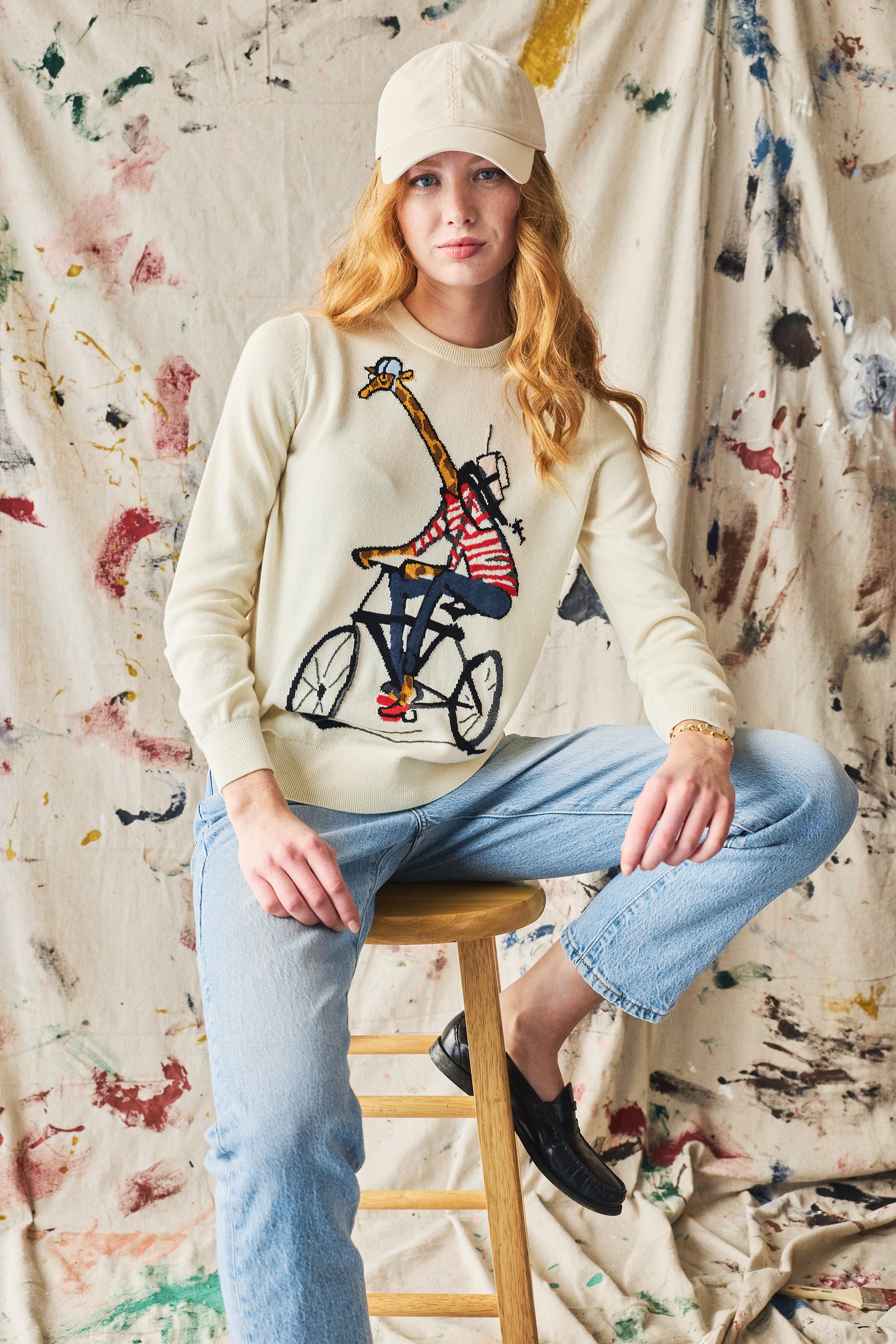 Person wearing a sweater with a design of a giraffe on a bike sitting on a stool against a textured wall.