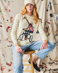 Person wearing a sweater with a design of a giraffe on a bike sitting on a stool against a textured wall.