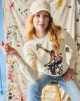 Person wearing a white sweater with a giraffe design, sitting on a stool against a colorful abstract background.