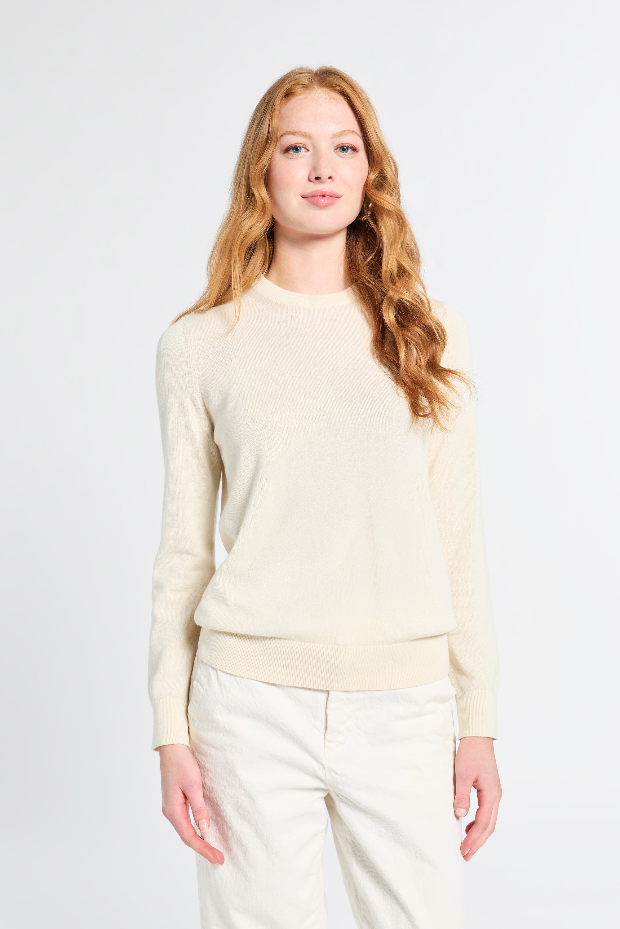 Woman modeling a long sleeve silk knit cream sweater on a plain backdrop