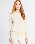 Woman modeling a long sleeve silk knit cream sweater on a plain backdrop