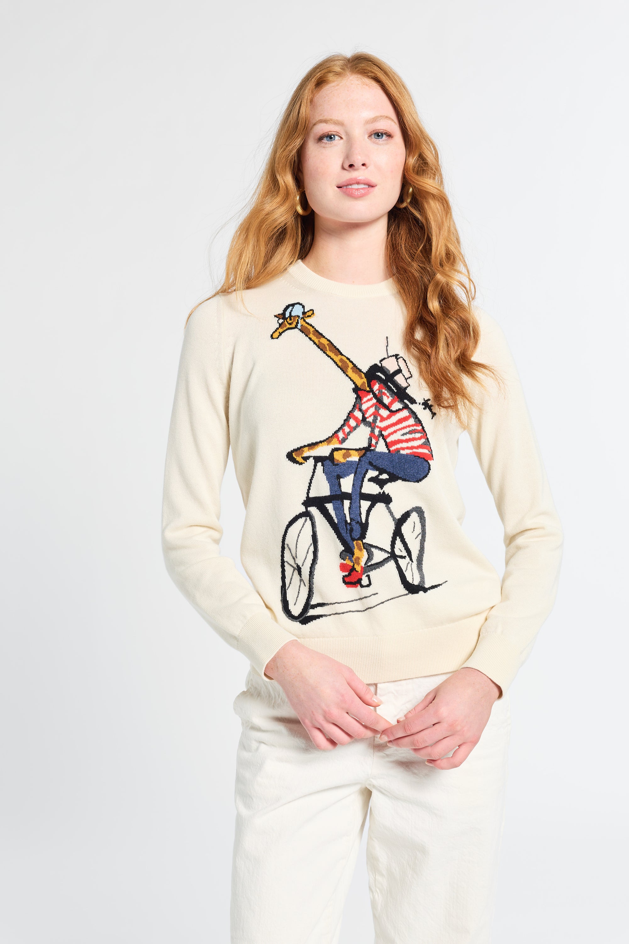 Woman wearing a cream sweater with a design of a giraffe on a bike on a white backdrop