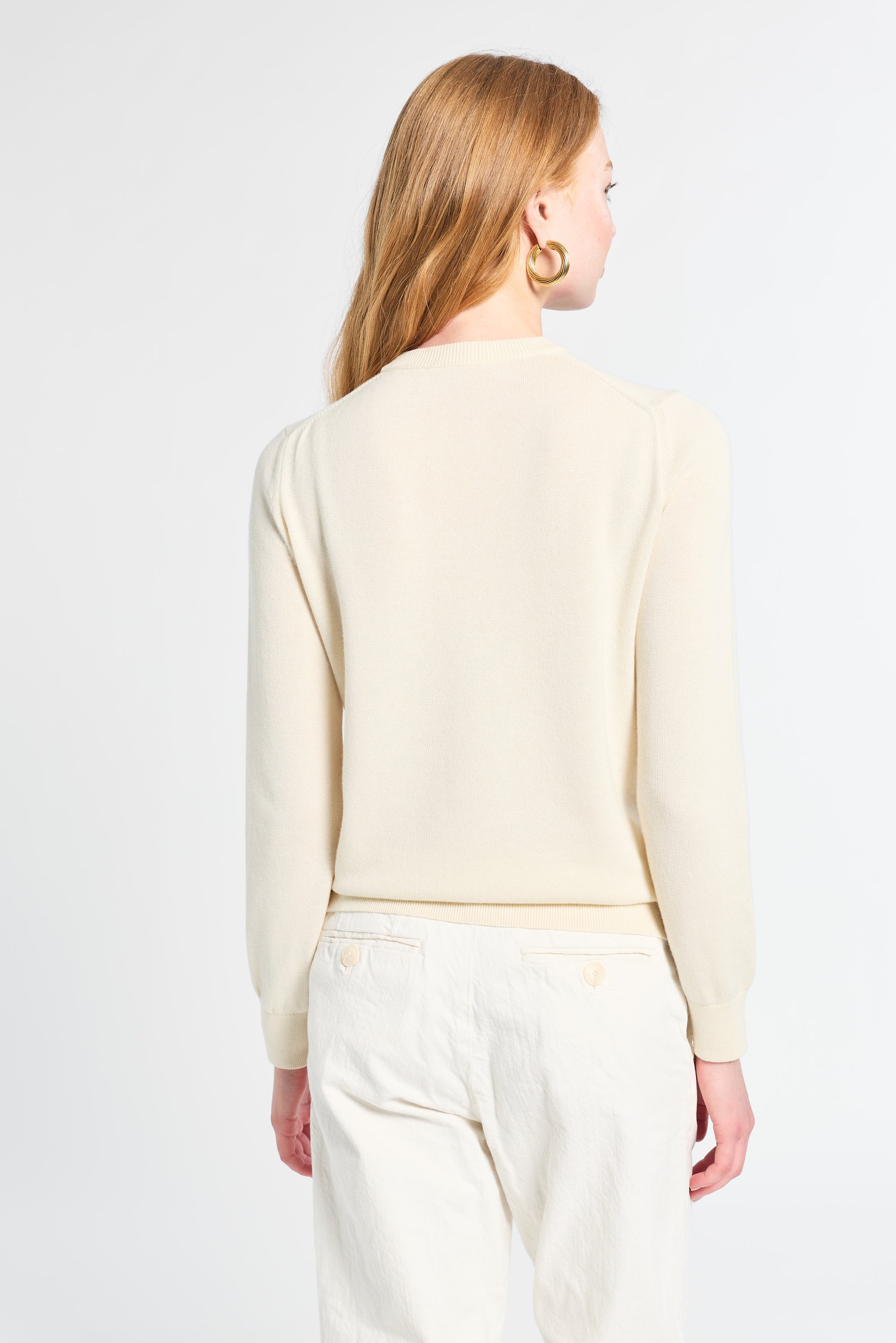 Woman wearing a light-colored sweater and white pants on a plain background