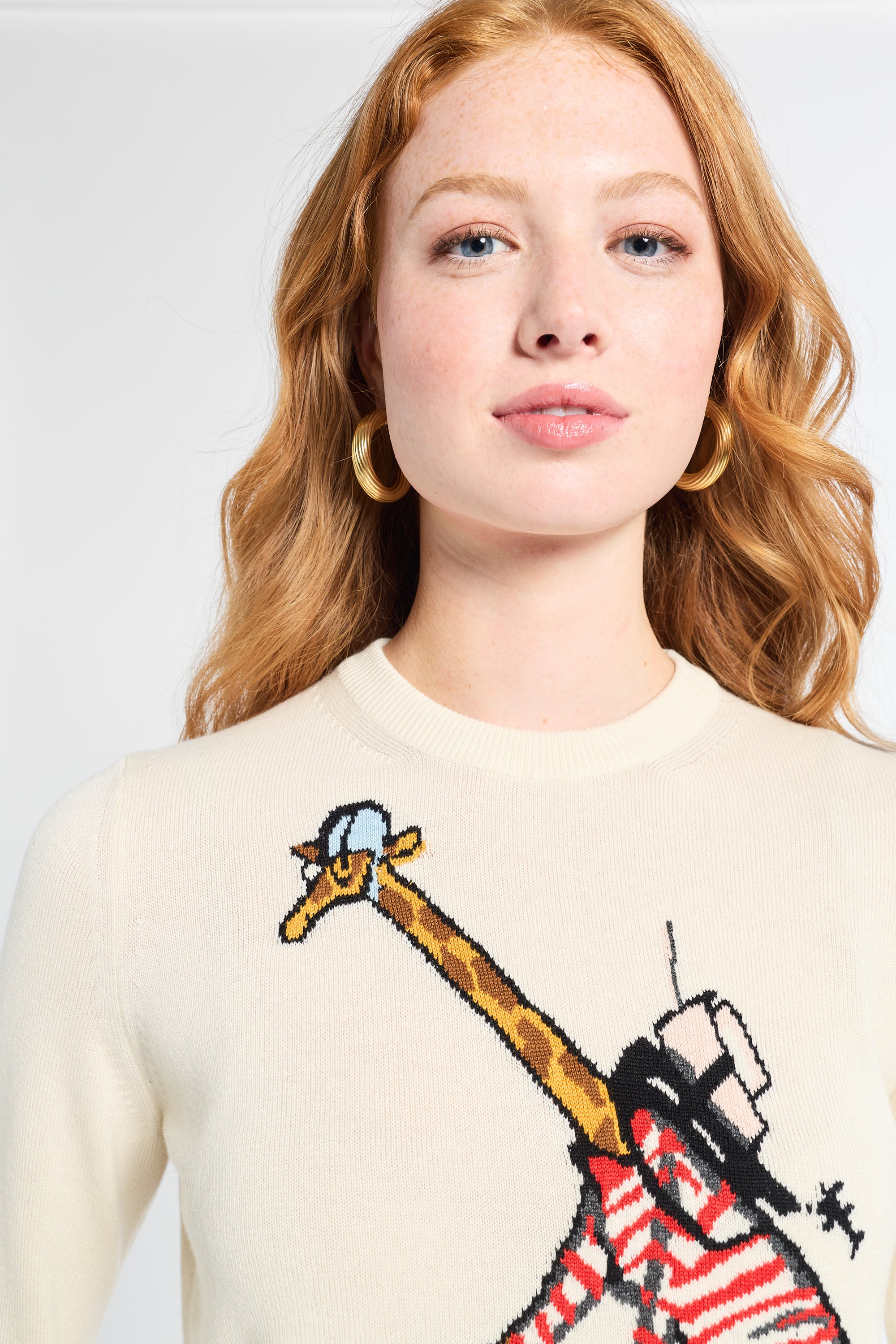 Woman wearing a sweater with a graphic design of a giraffe on a white backdrop.