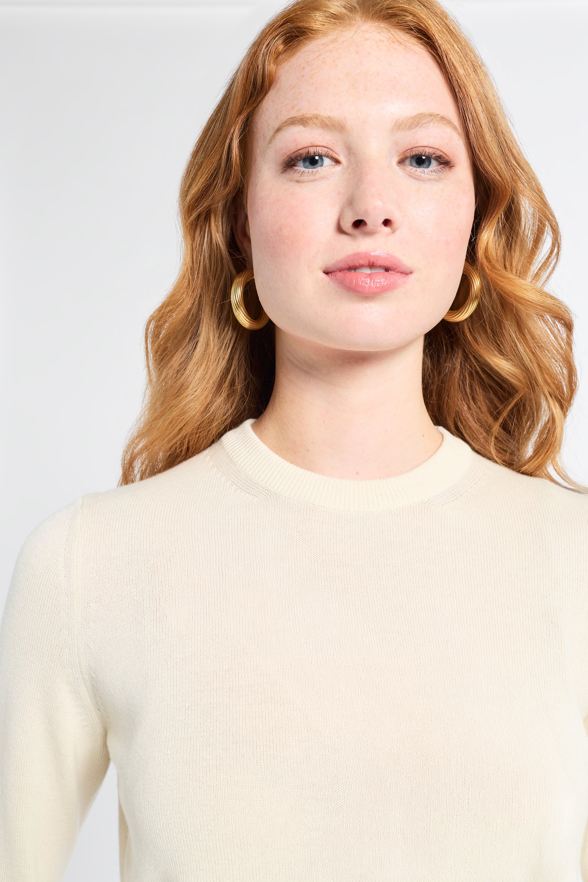Woman wearing a long sleeve cream cashmere sweater on a white backdrop