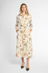 A woman modeling a long-sleeved midi shirt dress with a floral print on a cream background, paired with olive green pointed-toe flats, against a light gray studio background.