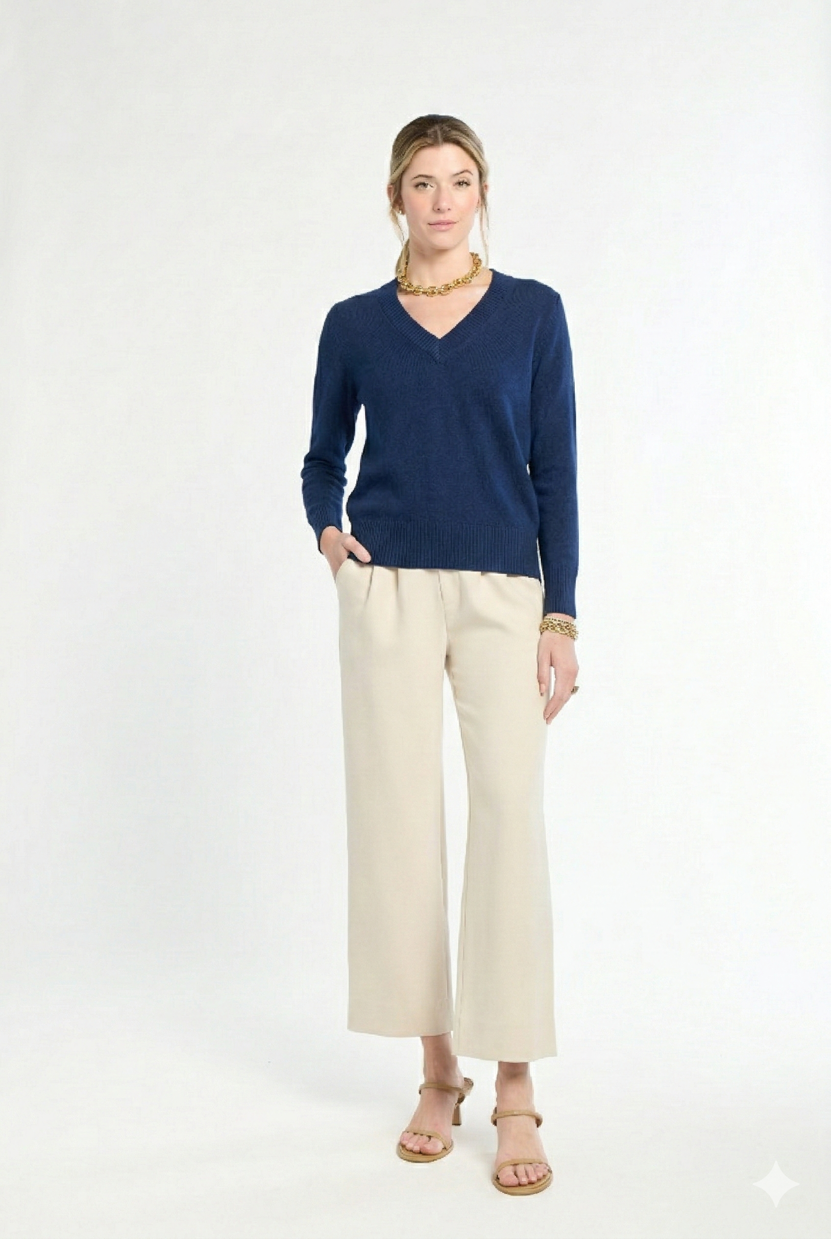 woman wearing navy v-neck sweater and cream pants on a white background
