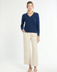 woman wearing navy v-neck sweater and cream pants on a white background