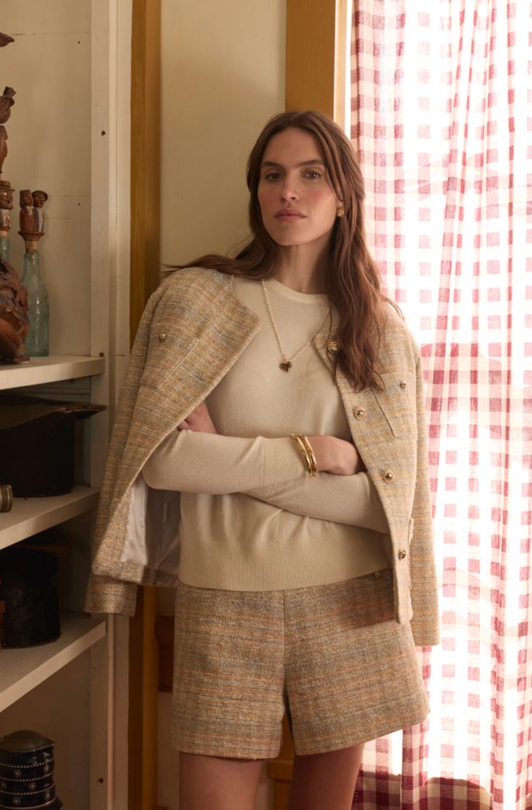 Woman wearing tweed shorts and blazer while standing in front of a window