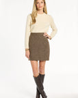 A woman modeling the Tobacco Tweed Meg Mini Skirt with a cream sweater and dark brown knee-high boots, front view, photographed against a plain white studio background.