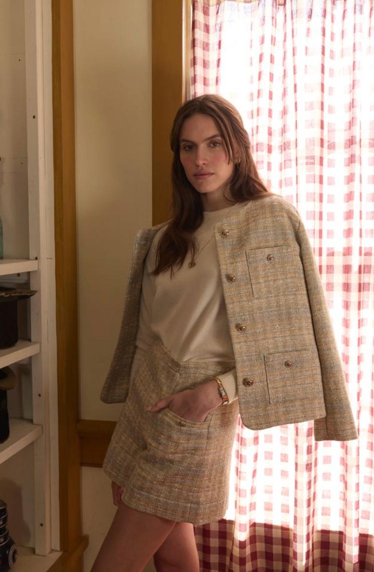 Woman wearing golden and light blue blazer in front of a gingham window curtain