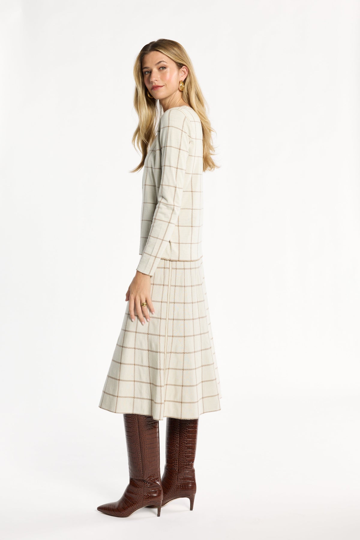 A woman modeling the cream side of the Chestnut Windowpane Plaid Reversible Crewneck with the matching skirt, side view, photographed against a plain white studio background.