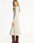 A woman modeling the cream side of the Chestnut Windowpane Plaid Reversible Crewneck with the matching skirt, side view, photographed against a plain white studio background.