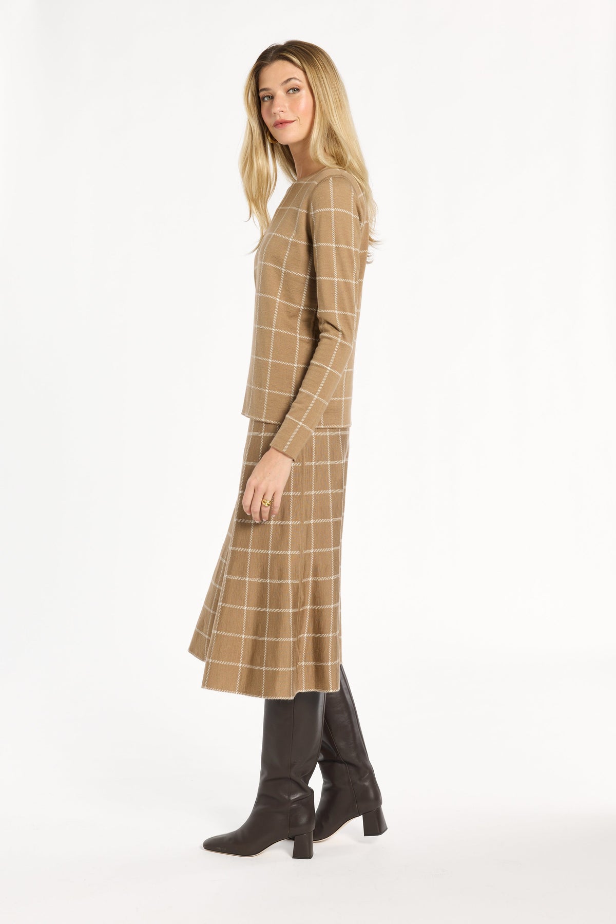 A woman modeling the chestnut side of the Windowpane Plaid Reversible Crewneck with the matching skirt, side view, photographed against a plain white studio background.