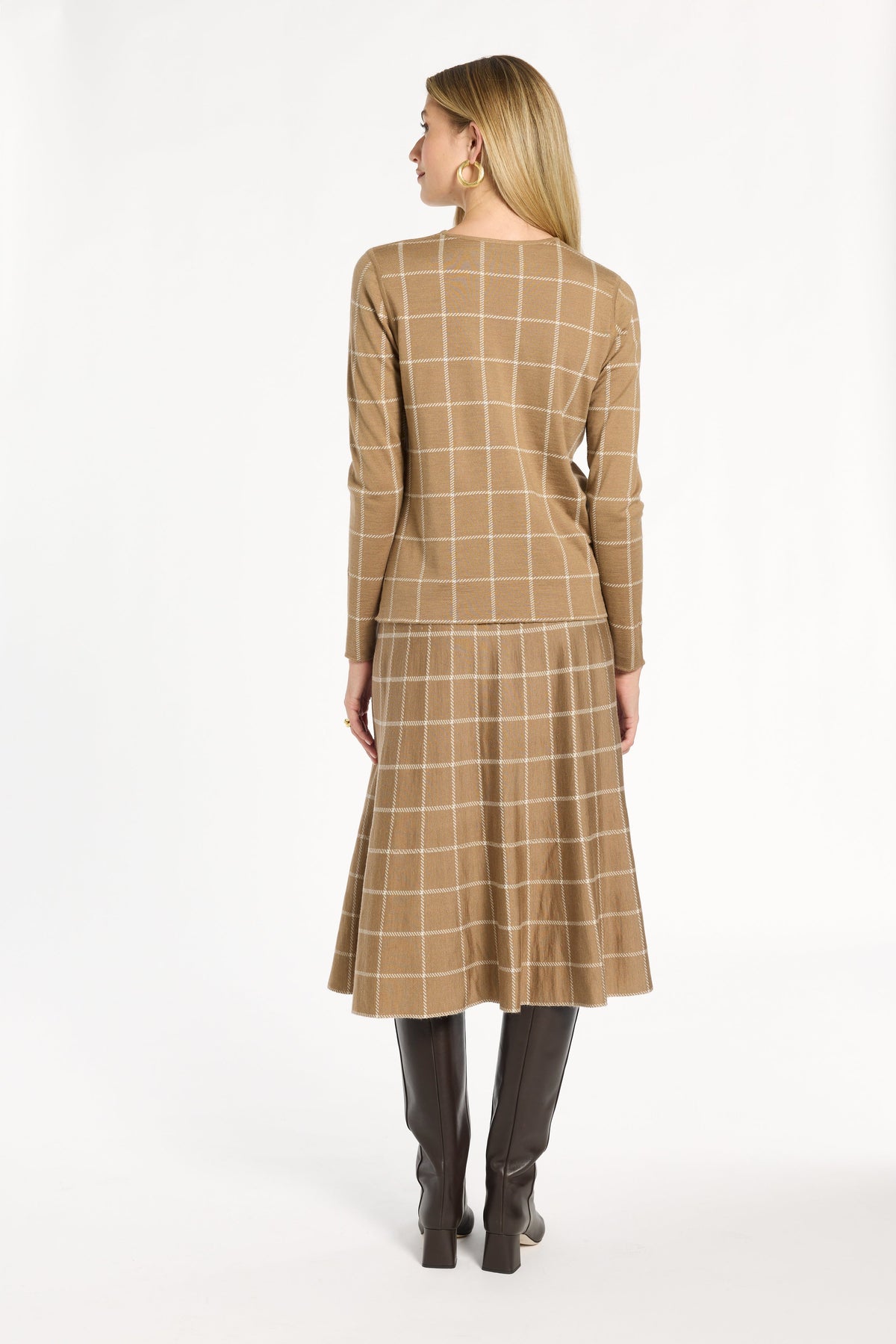 A woman modeling the chestnut side of the Windowpane Plaid Reversible Crewneck with the matching skirt, back view, photographed against a plain white studio background.