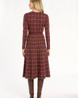 A woman modeling the cranberry side of the Windowpane Plaid Reversible Flared Skirt with the matching crewneck and brown boots, back view, photographed against a plain white studio background.