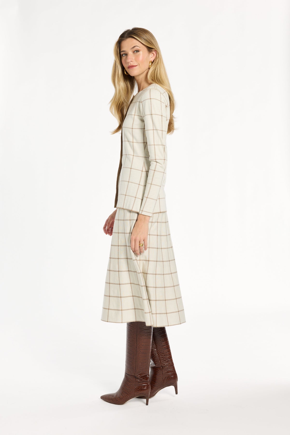A woman modeling the cream side of the Reversible Knit Jacket with the matching windowpane skirt, side view, photographed against a plain white studio background.