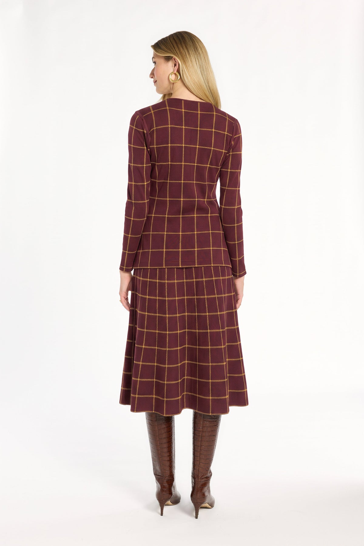 A woman modeling the cranberry side of the Windowpane Plaid Reversible Knit Jacket with the matching skirt, back view, photographed against a plain white studio background.