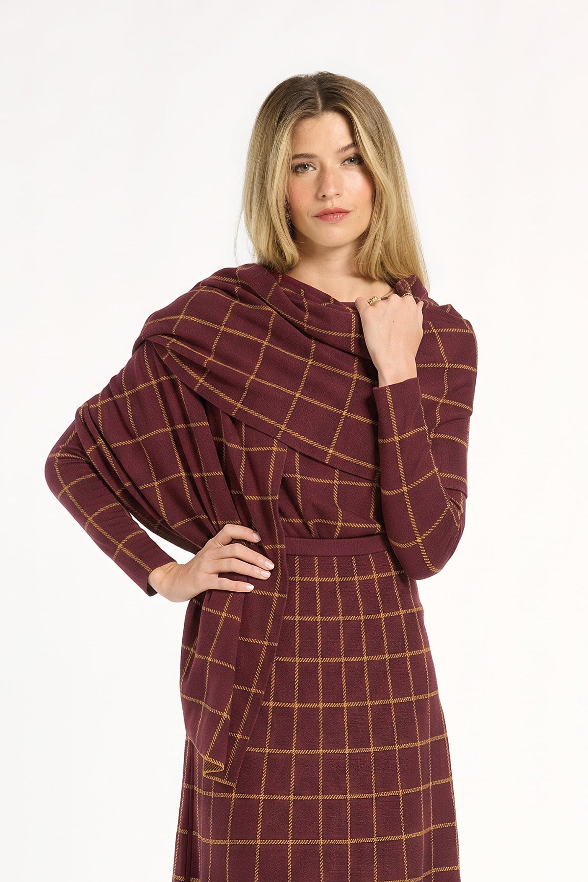 A woman modeling the cranberry side of the Windowpane Plaid Reversible Wrap draped over the matching skirt and crewneck, front view, photographed against a plain white studio background.