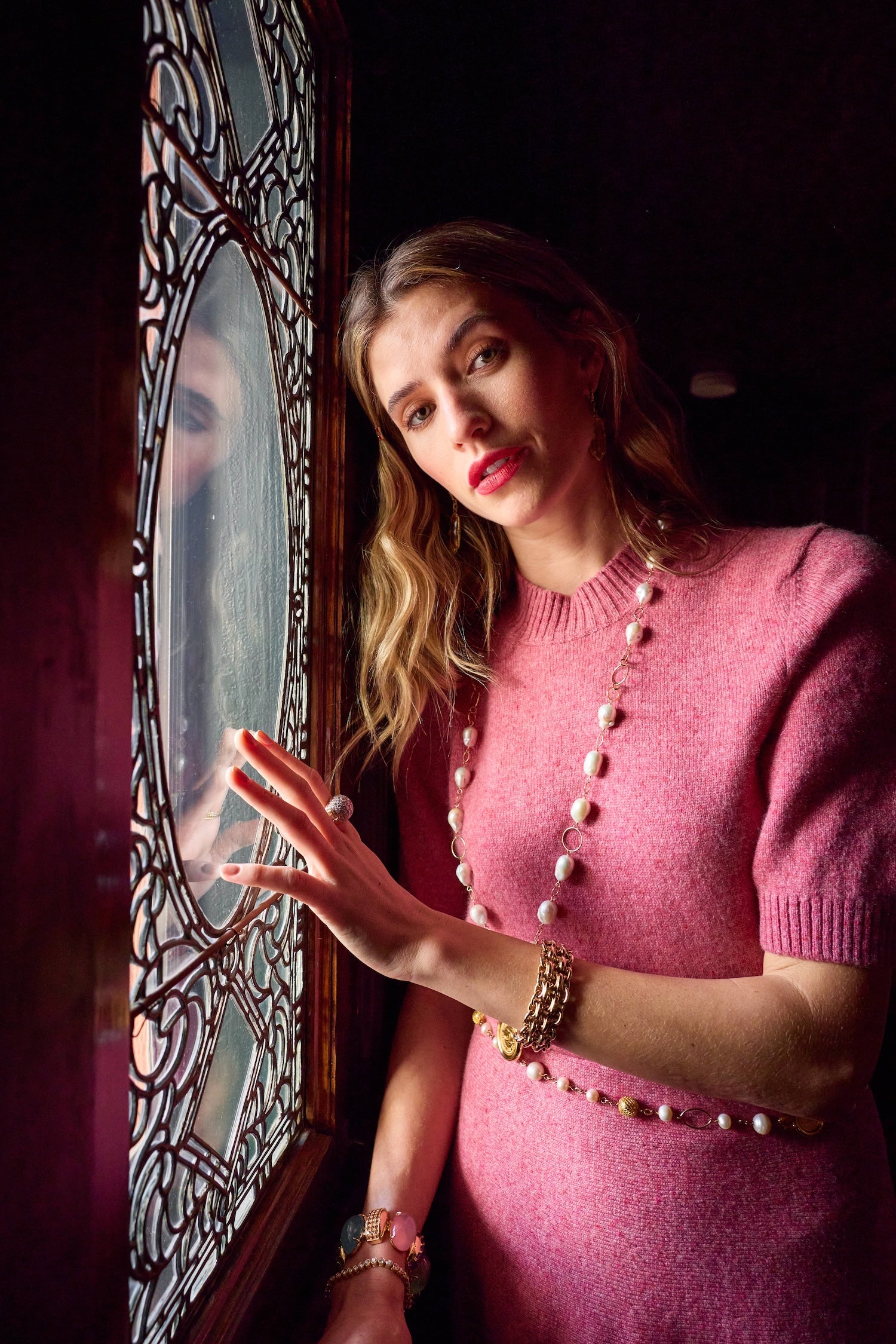 Woman in a pink dress standing near a stained glass window