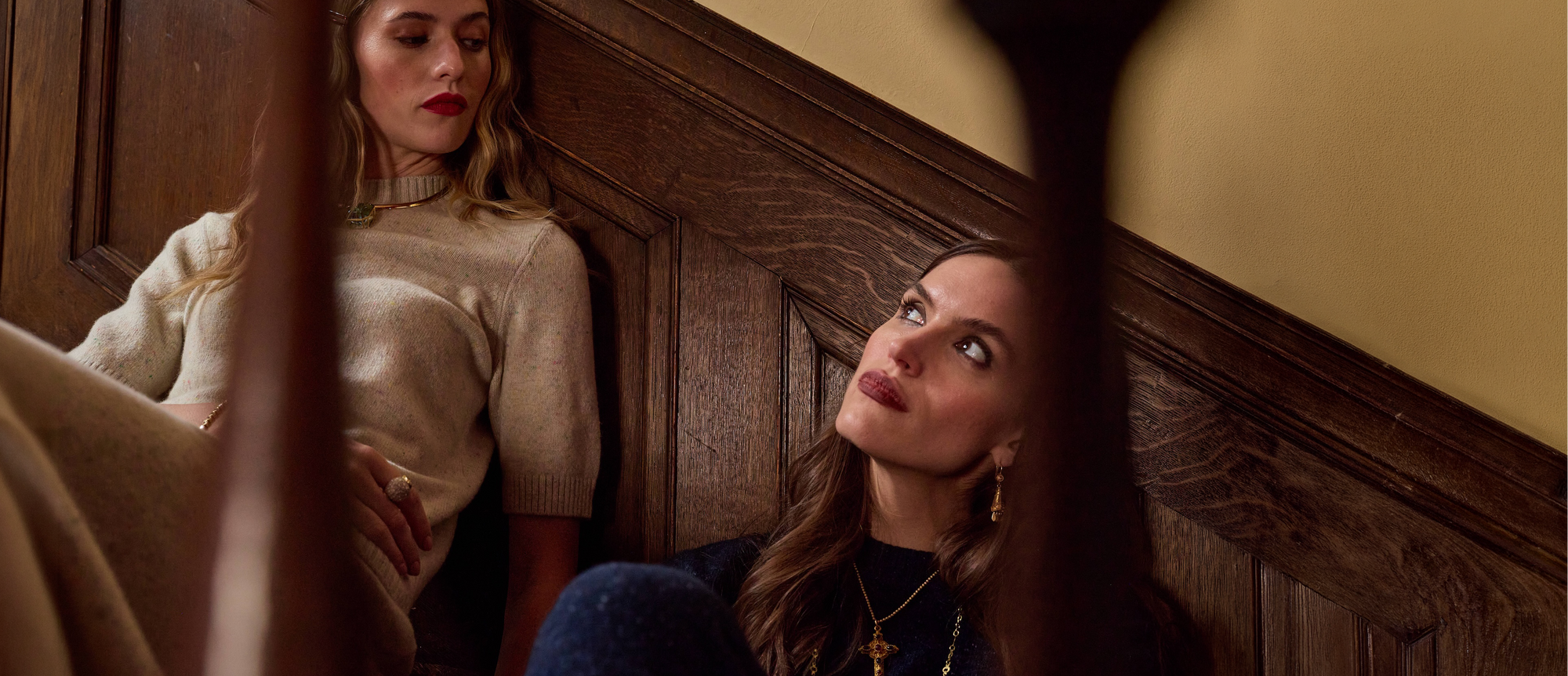 Two women sitting on a staircase with wooden paneling.