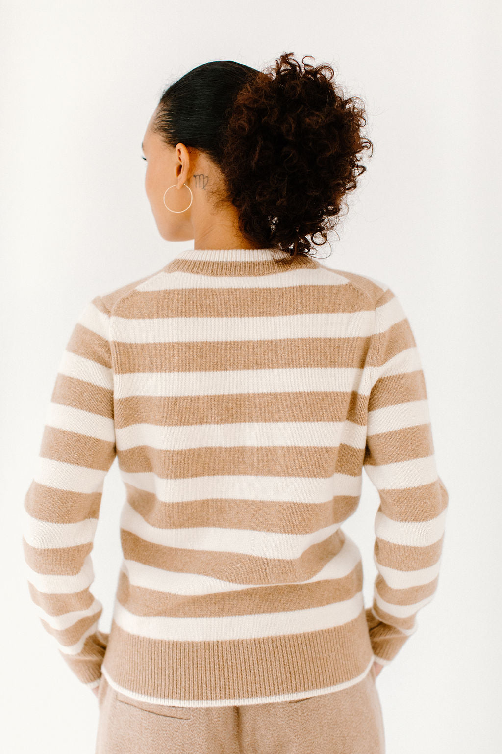 Back view of model wearing the Classic Striped Cashmere Crew in camel/cream stripes, paired with matching camel trousers.