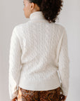 Back view of model wearing the Cream Cable-Knit Turtleneck sweater paired with paisley patterned pants, showcasing the sweater's texture.